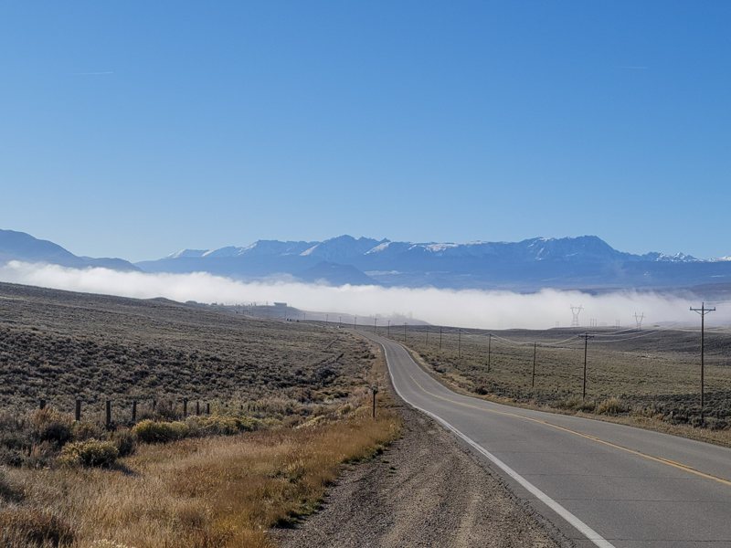 Empty road leading toward fog and a mountain range