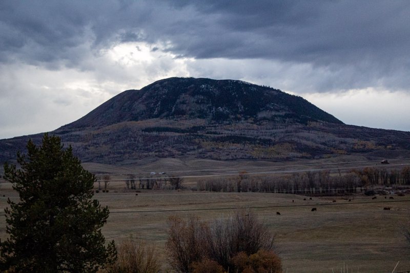 Dark dome mountain under storm clouds over grassland