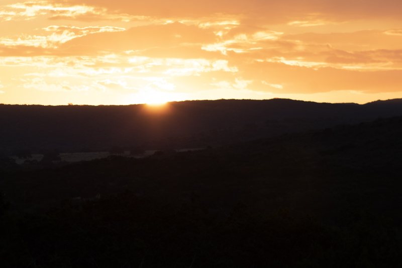 Sun setting behind a dark ridge under golden clouds