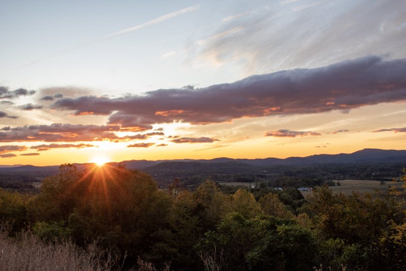 Sun setting over rolling wooded hills and valley farmland