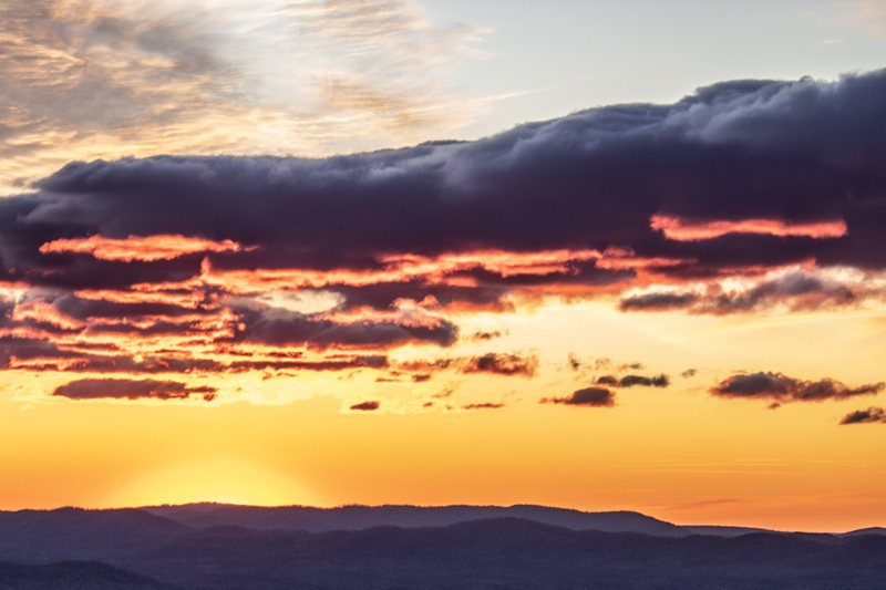 Dark clouds over a golden sunset sky above a ridgeline